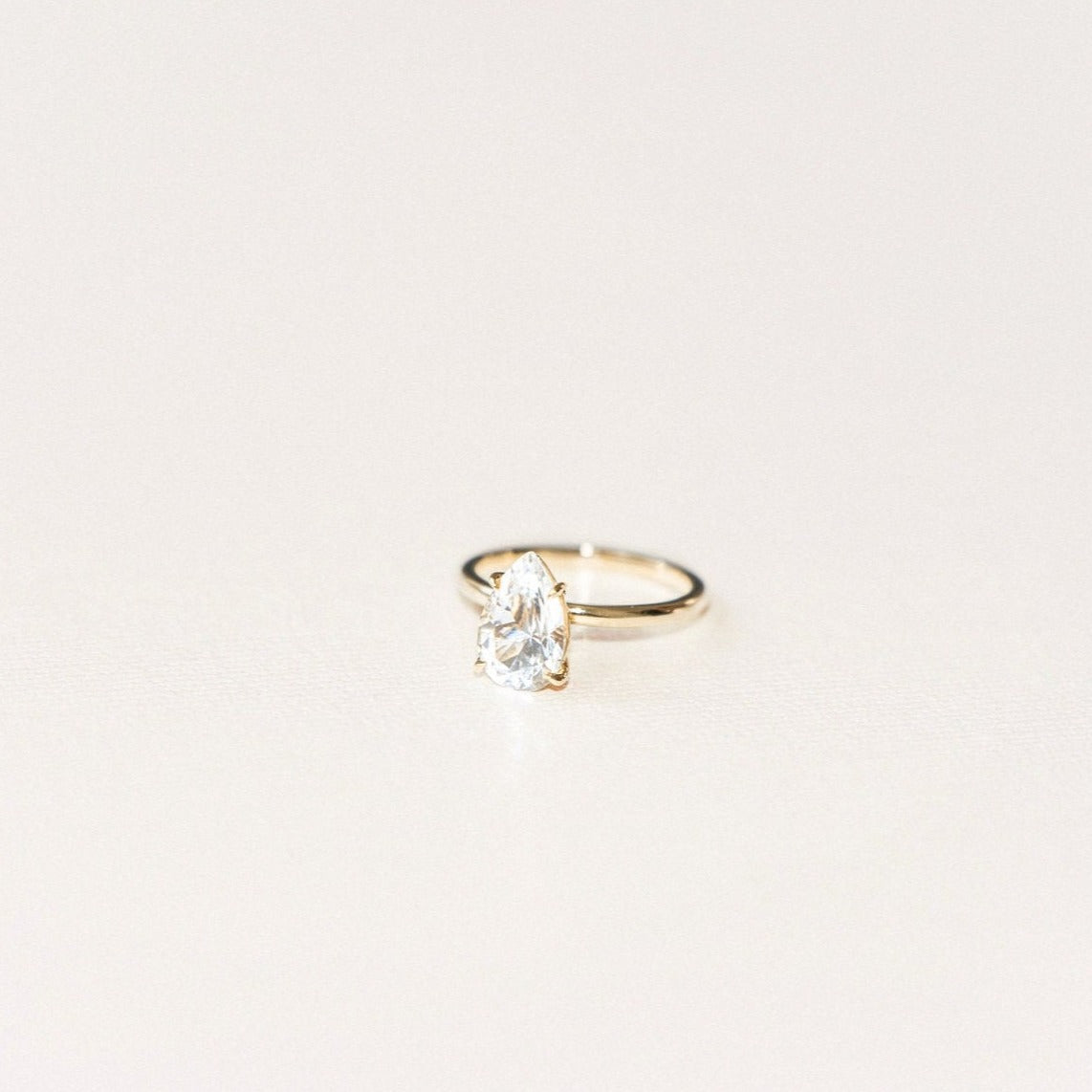 Piqued ring featuring a pear-shaped white sapphire solitaire set on a slim yellow gold band.