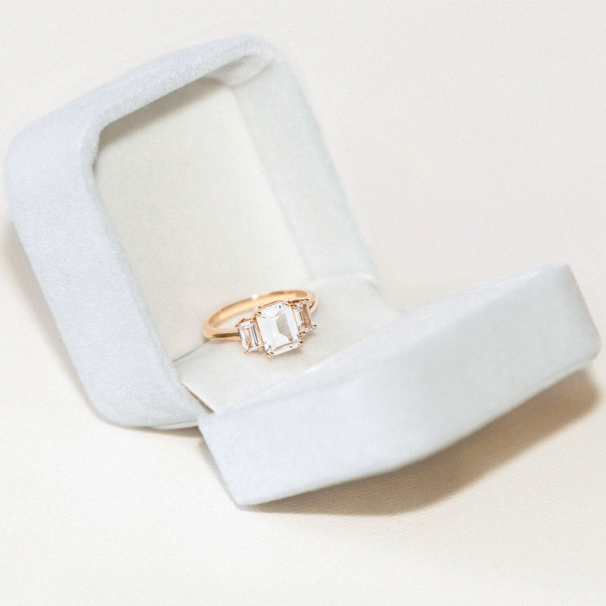 emerald cut sapphire engagement ring with diamond side stones in gold band displayed in white velvet ring box