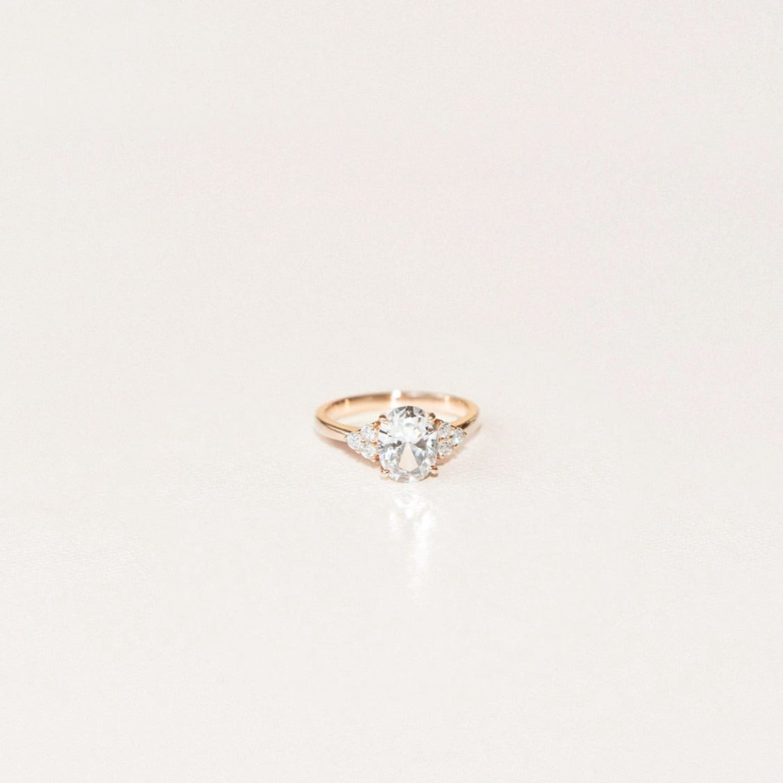 Oval white sapphire engagement ring with side diamond accents in yellow gold.