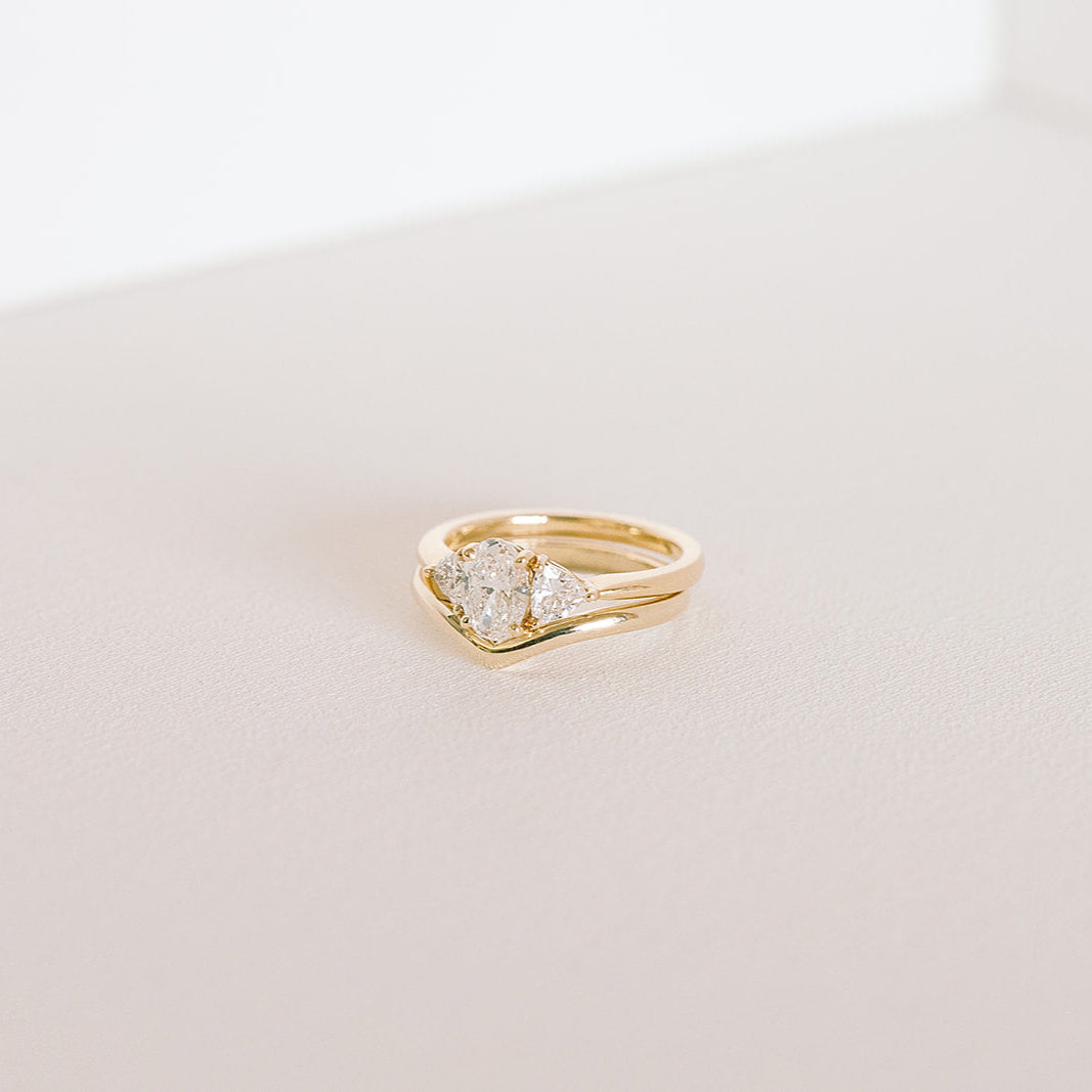 Gold curved wedding band stacked beneath a three-stone diamond ring, photographed on a light background.