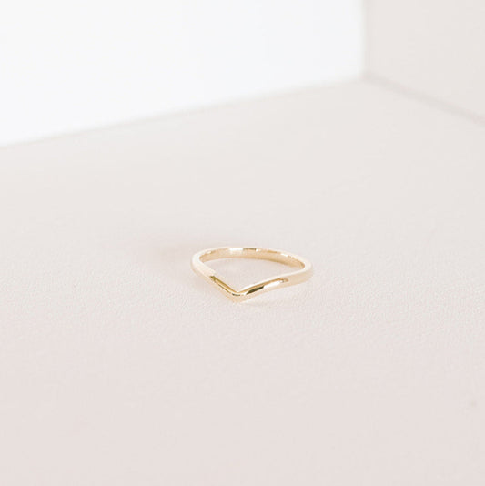 Minimal curved gold band displayed on a light surface.