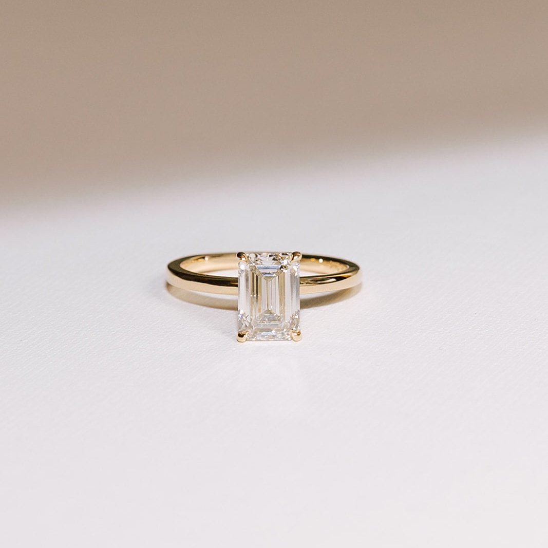 Enamoured engagement ring featuring a 2.05-carat emerald-cut lab diamond set in a 14k yellow gold band, photographed against a light background.