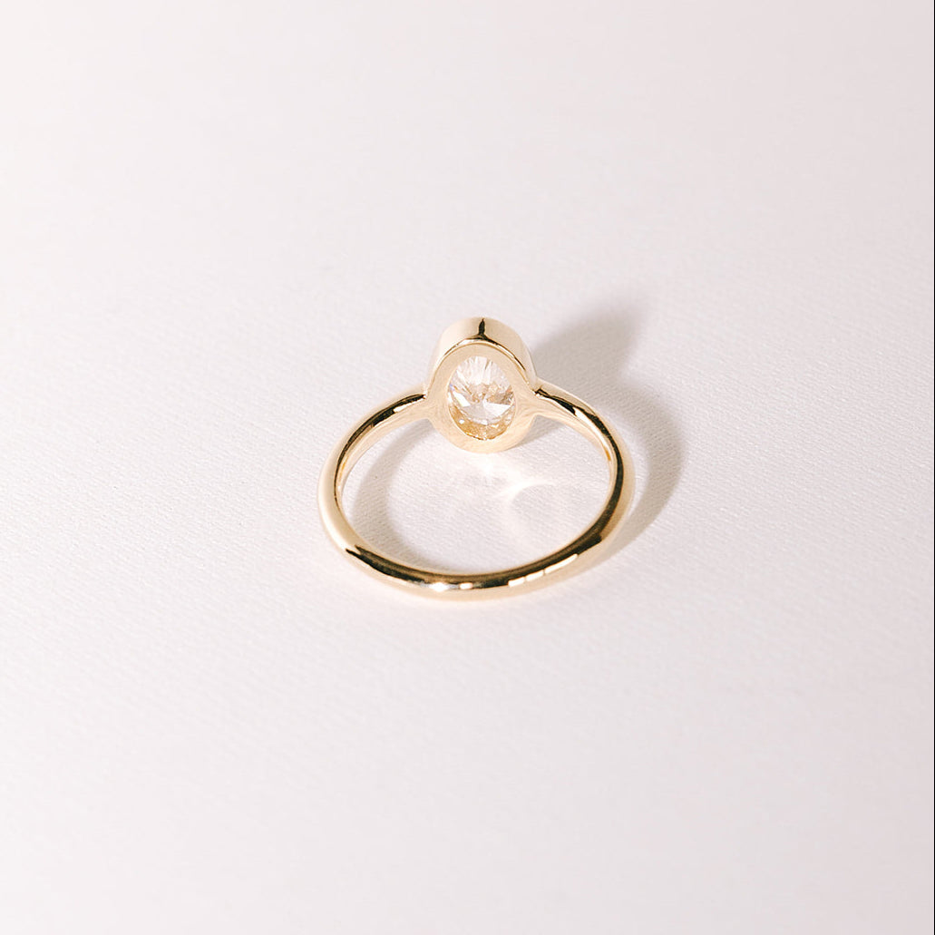 Oval lab-grown diamond bezel engagement ring in yellow gold band, back view of setting on light surface.