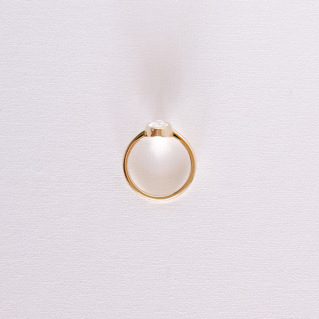 Oval lab-grown diamond bezel engagement ring in yellow gold band, front view on light background.