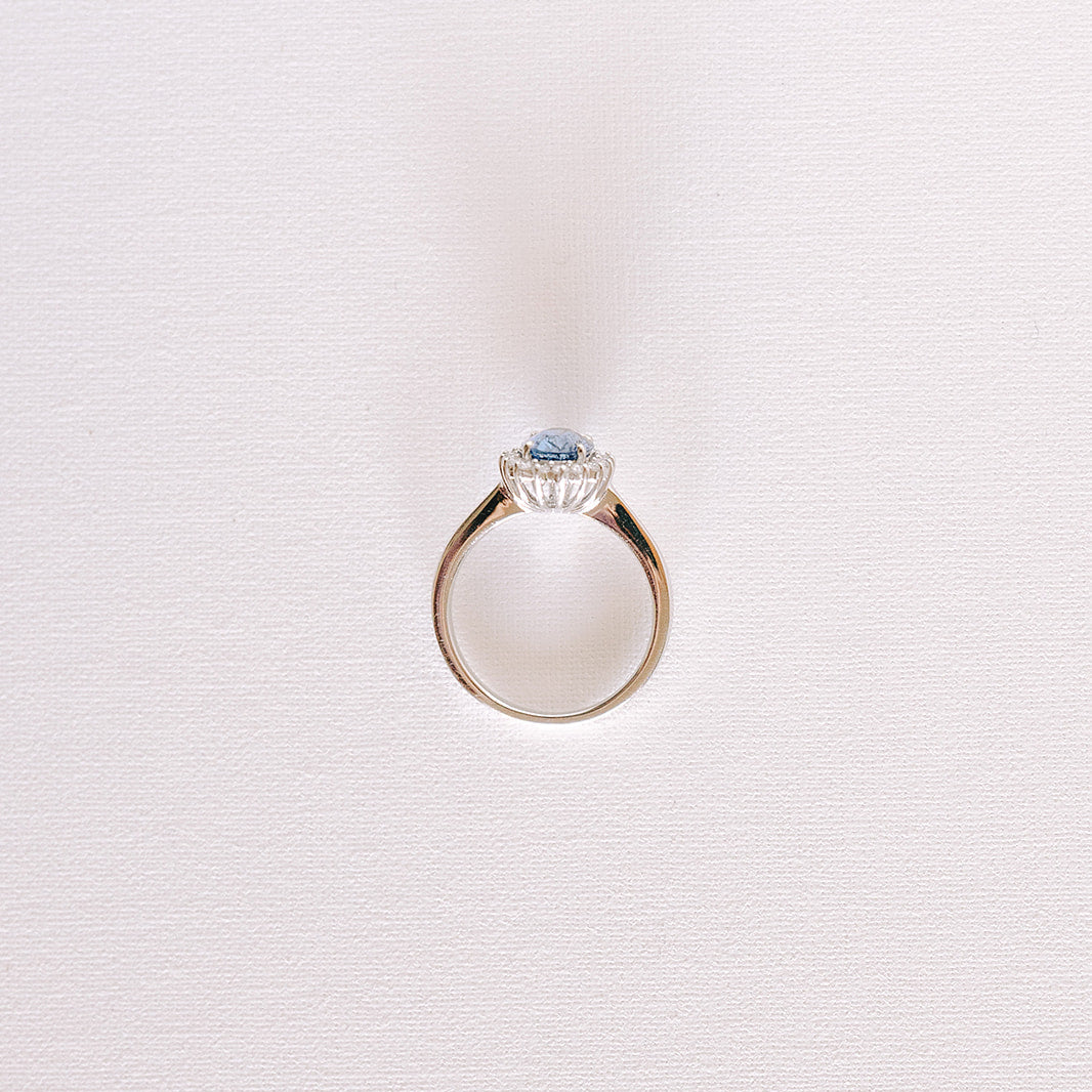 Blue oval sapphire ring with diamond halo in white gold band, front view.