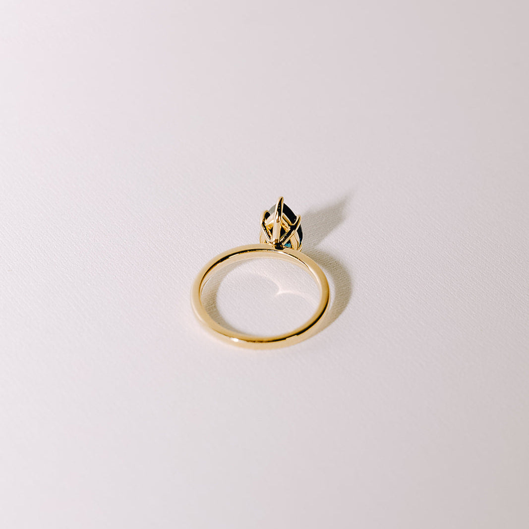 Teal pear-shaped sapphire solitaire ring in yellow gold band, angled back view showing prong setting.