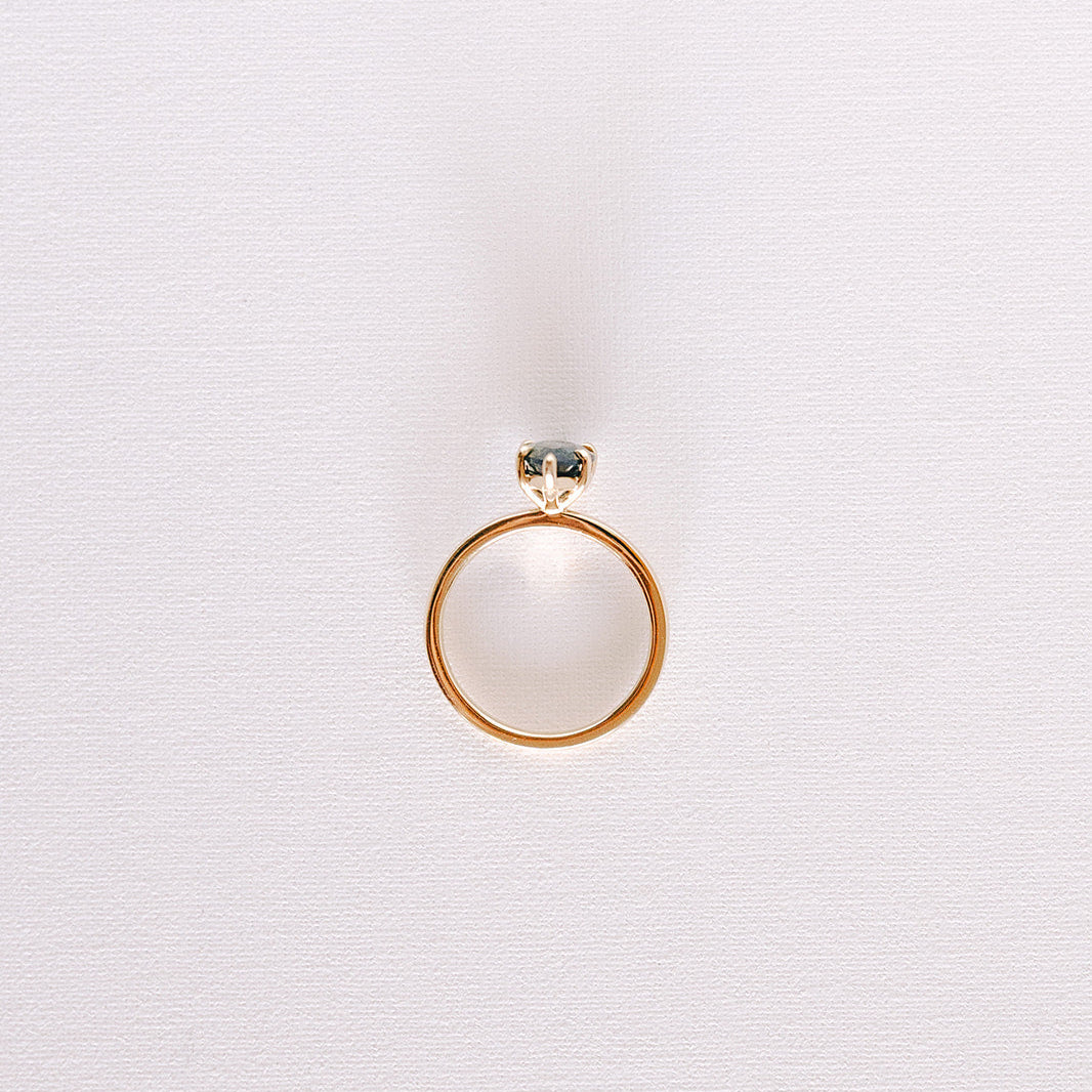 Teal pear-shaped sapphire solitaire ring in yellow gold band, top-down view on light background.