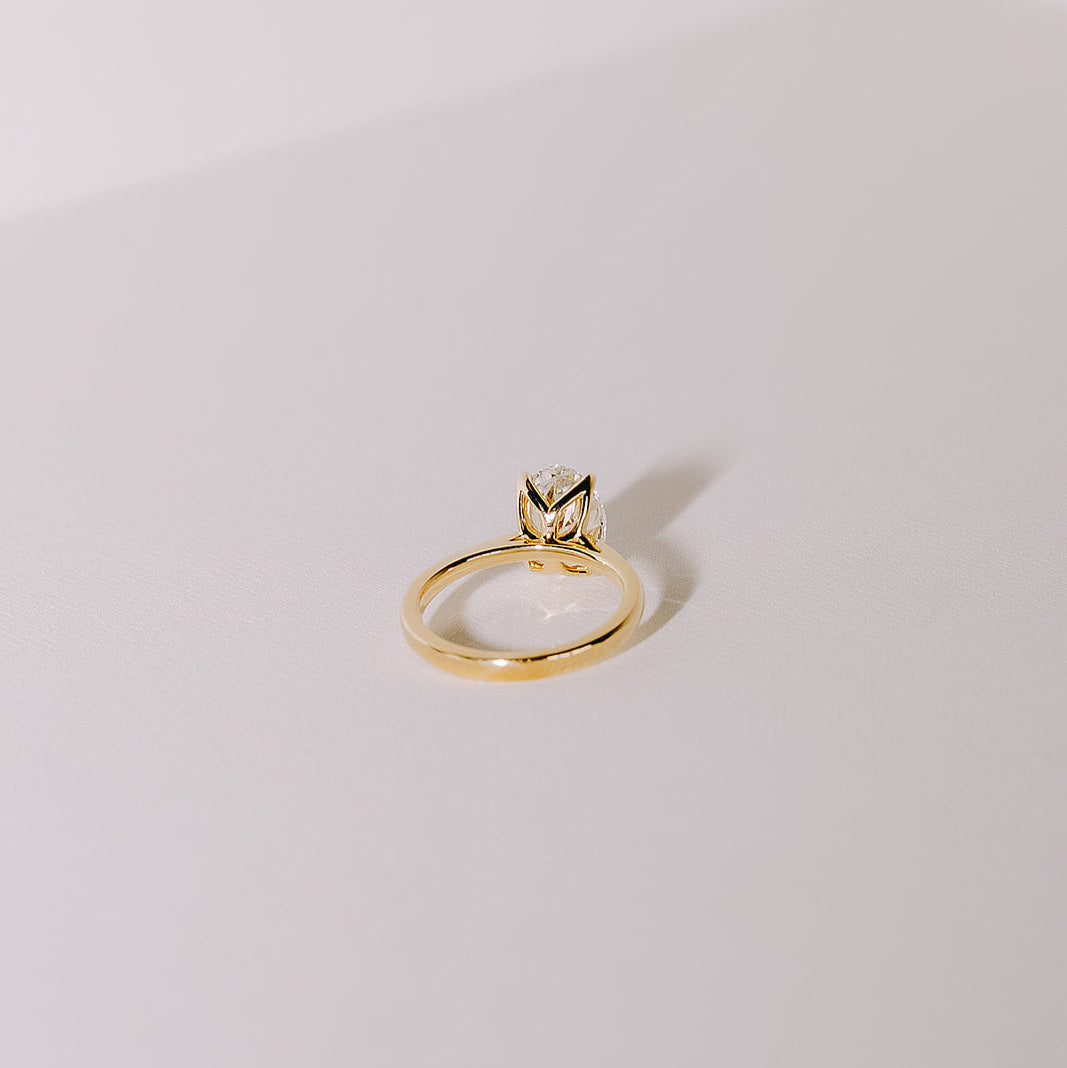 Oval lab-grown diamond engagement ring in yellow gold cathedral setting, angled back view on light background.