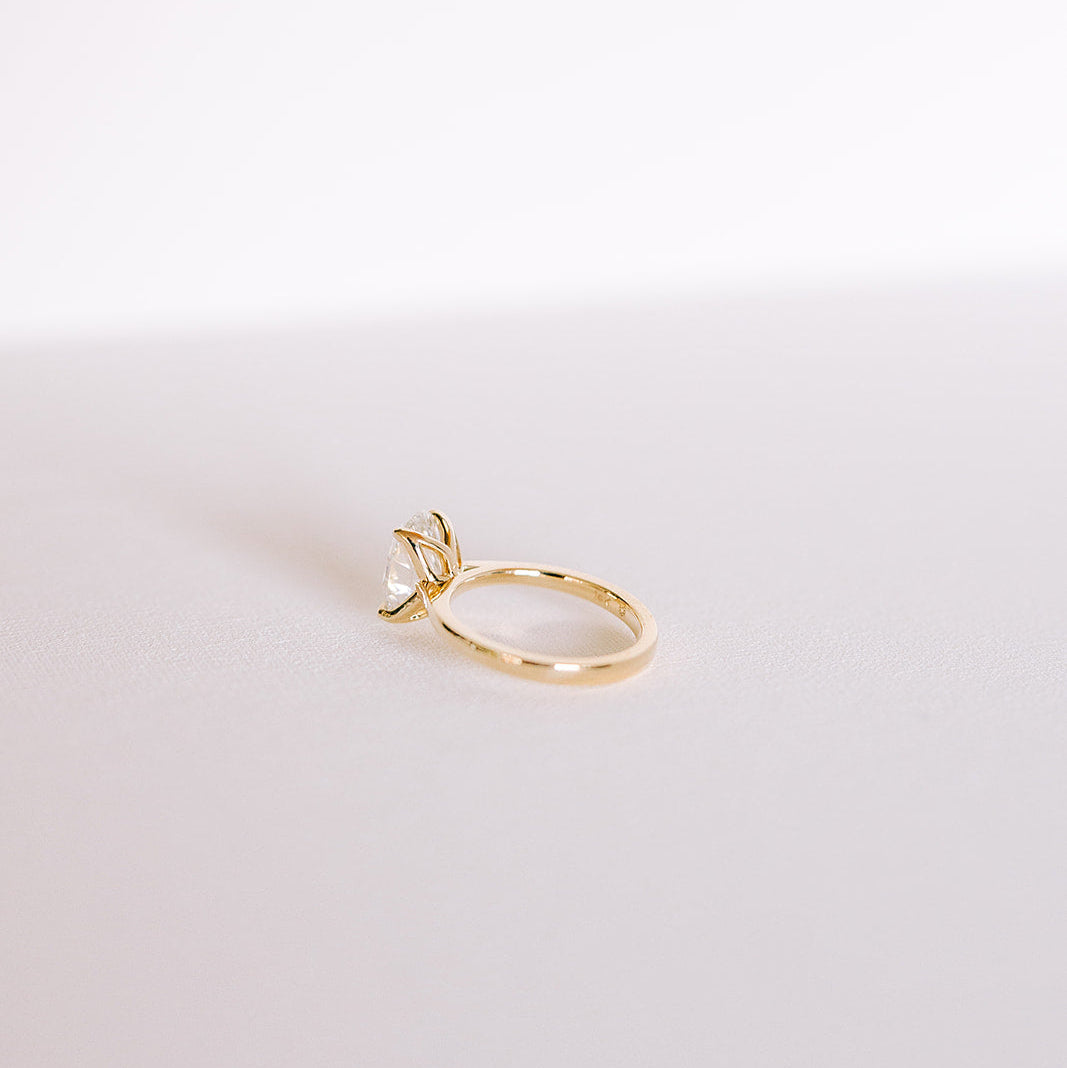 Oval lab-grown diamond engagement ring in yellow gold cathedral setting, side view on light surface.