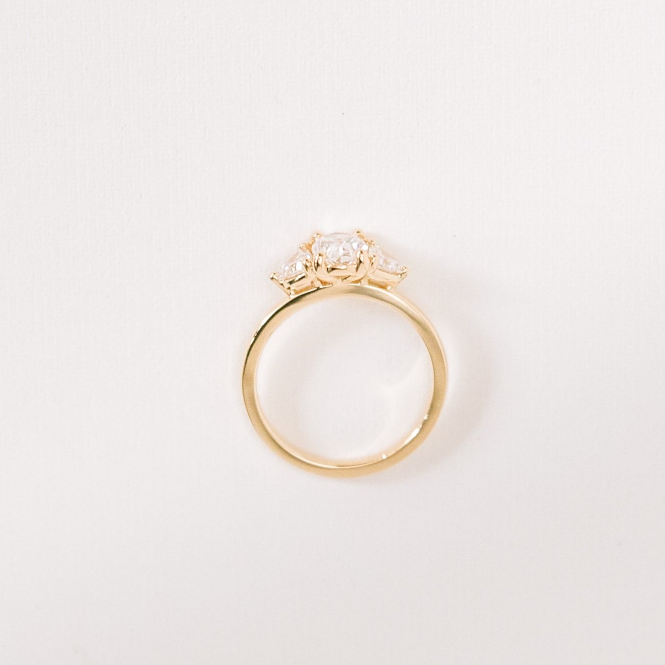 Euphoric High three-stone ring with an oval lab-grown diamond and two trilliant side diamonds in a yellow gold band, photographed from the side to show its medium-high setting.