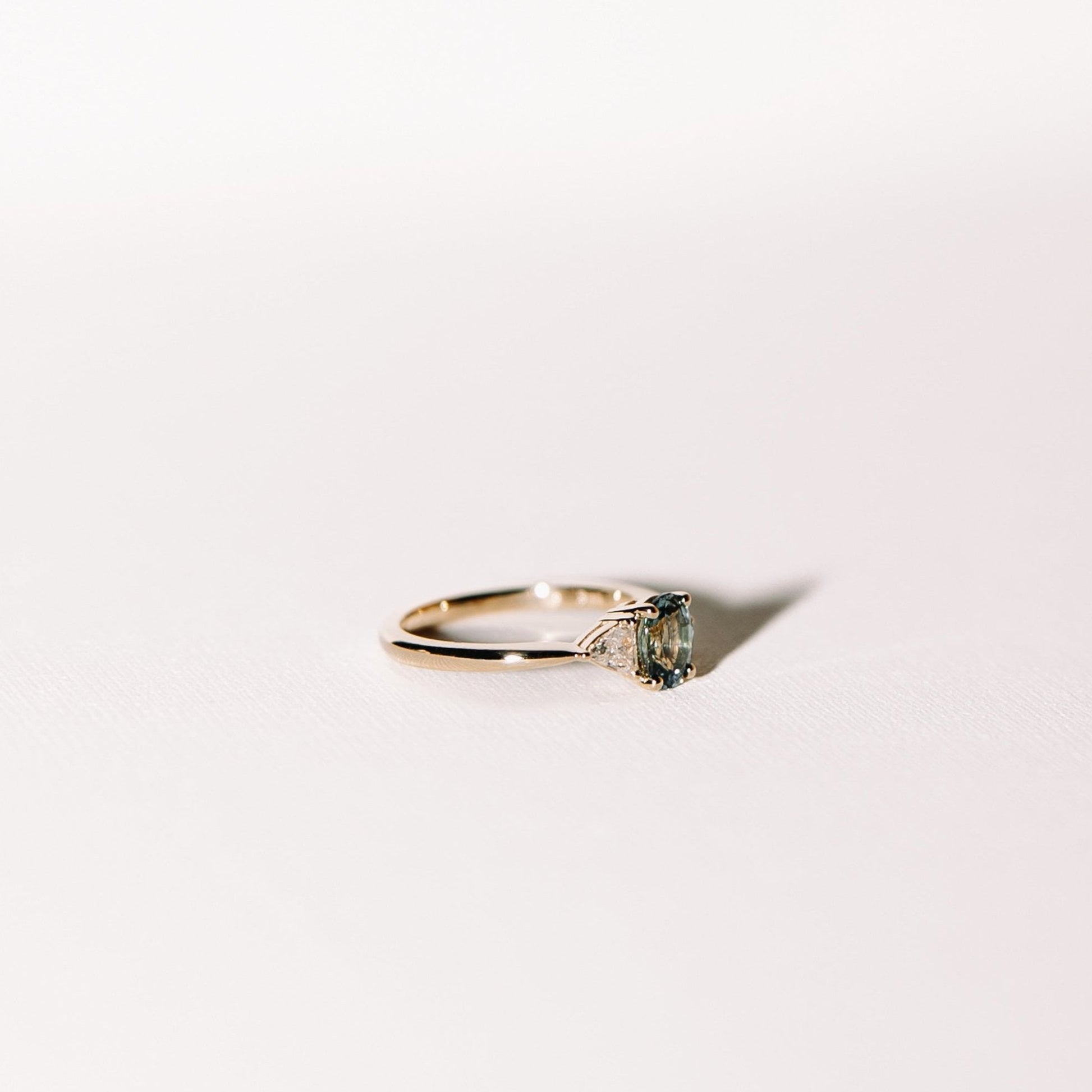 Euphoric Teal trilogy engagement ring with oval teal sapphire and trilliant lab diamonds in 14k yellow gold, alternate side profile view.