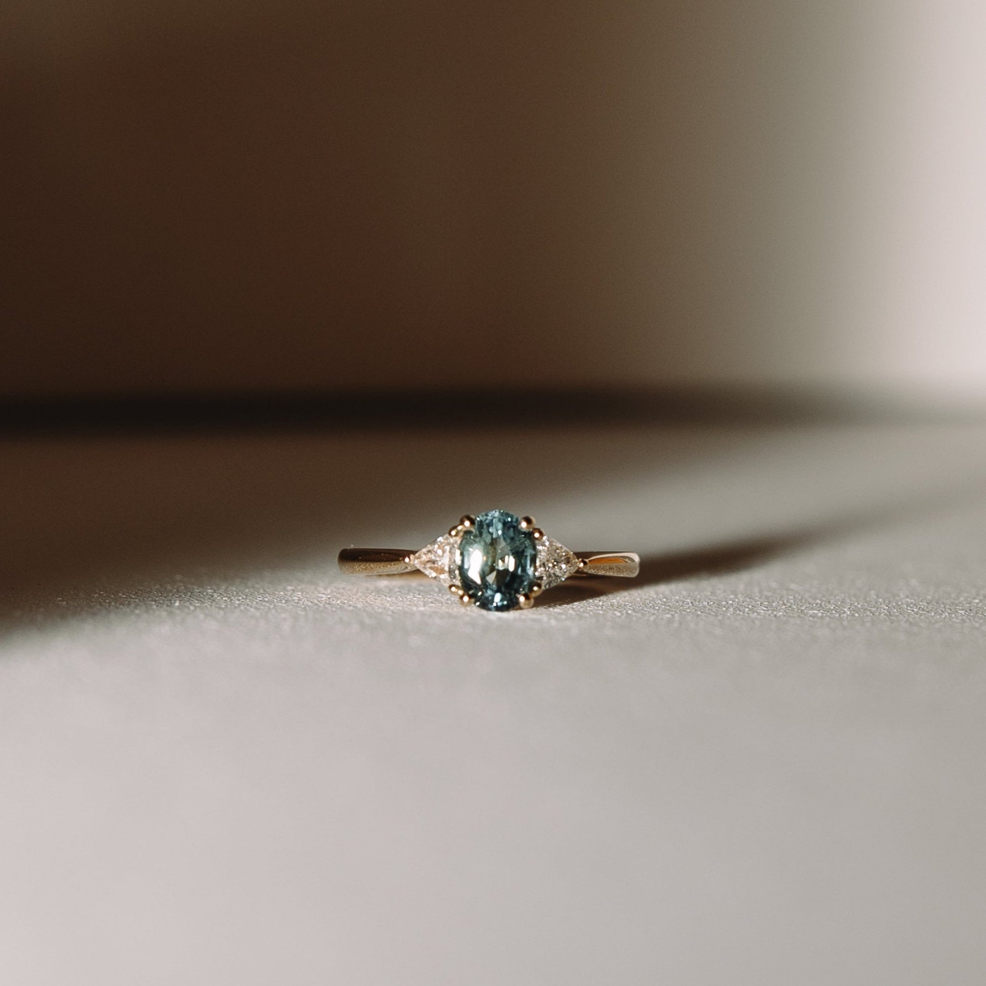 Euphoric Teal sapphire and diamond trilogy engagement ring with oval teal sapphire and trilliant lab diamonds in 14k yellow gold, front view.