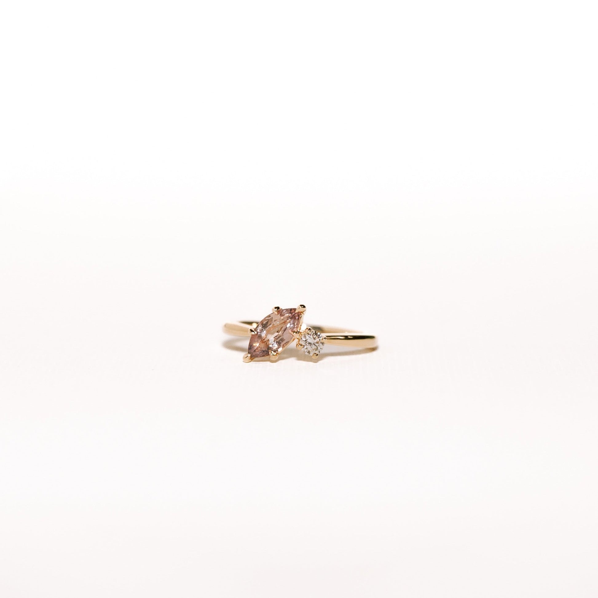 Dusk till Dawn toi et moi ring with a peach-champagne marquise sapphire and round diamond on a yellow gold band, photographed under bright full lighting.