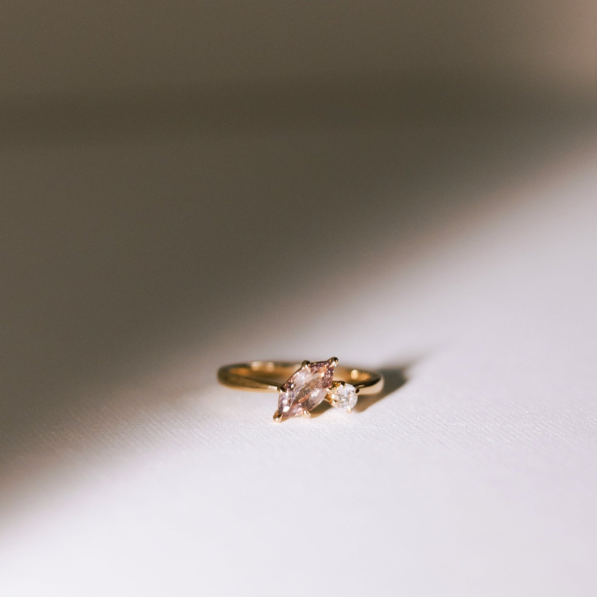 Dusk till Dawn toi et moi ring with a marquise peach-champagne sapphire and a round diamond set in a 14k yellow gold band, photographed on a soft white surface.
