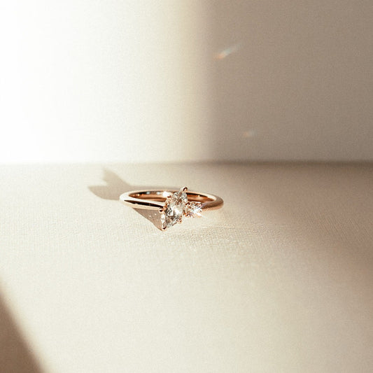 Moonlit Tide toi et moi ring with a marquise-cut green sapphire and round diamond, photographed in warm natural light on a textured surface.