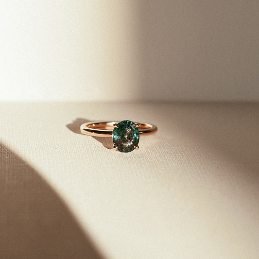 Montana Sky ring featuring an oval teal sapphire on a yellow gold band, captured from the front angle with warm natural lighting and soft shadows.