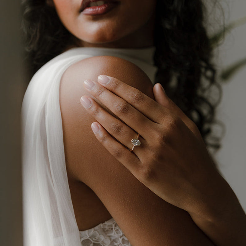 Model with hand resting on shoulder wearing Still — an oval lab diamond bezel engagement ring in yellow gold.