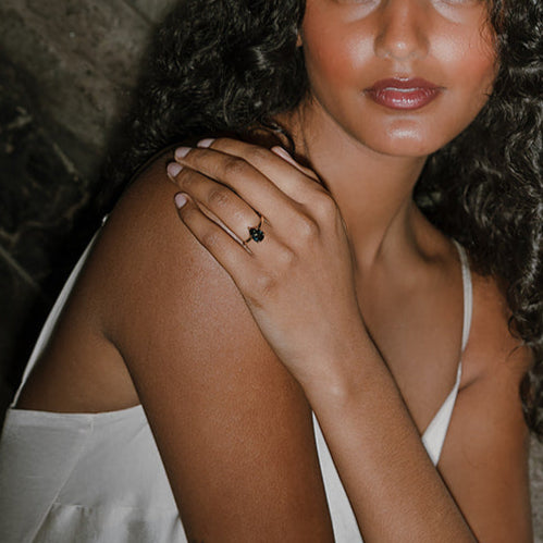 Model wearing Ma Folie’s Swell ring. A teal pear sapphire solitaire in 14k yellow gold, shown on hand against a natural textured background.