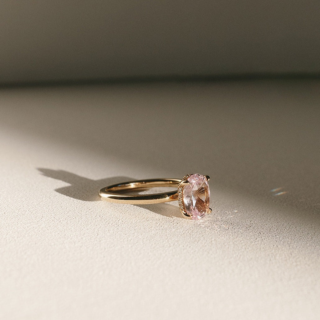 Sweet Romance oval pink sapphire solitaire ring in 14k yellow gold, side view with natural light shadow.