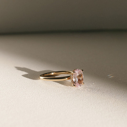 Sweet Romance oval pink sapphire solitaire ring in 14k yellow gold, side view with natural light shadow.