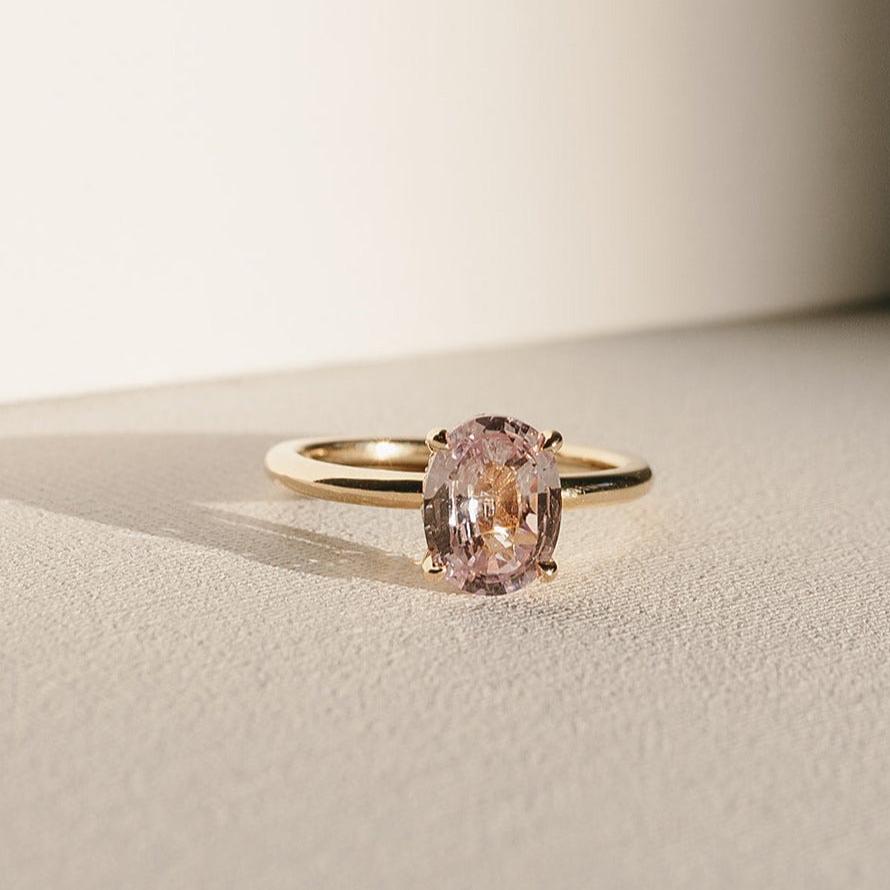 Sweet Romance engagement ring with oval pink sapphire set in 14k yellow gold, solitaire design in natural light.