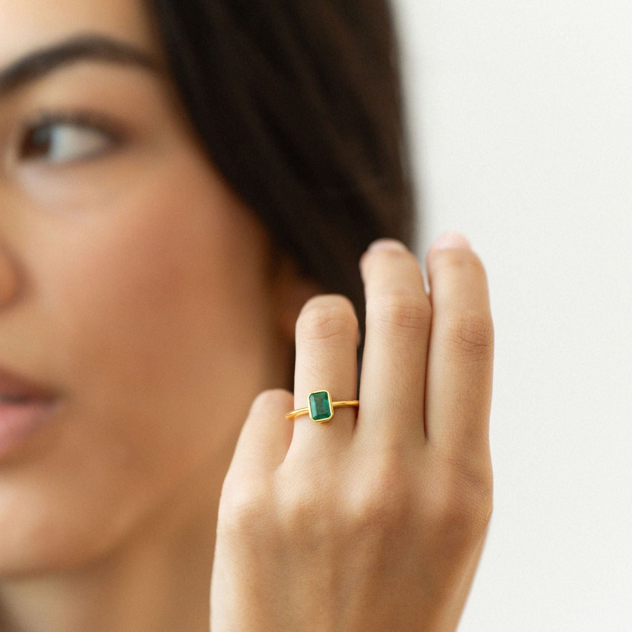 Emerald engagement ring with bezel setting in yellow gold, inspired by art deco design.