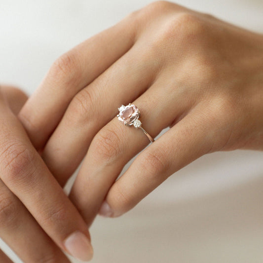 Light pink oval sapphire engagement ring with diamond side stones in white gold.