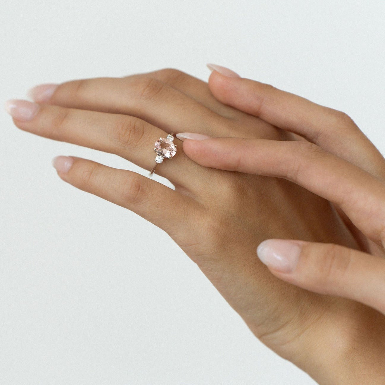 Oval light pink sapphire engagement ring with diamond side stones in white gold.