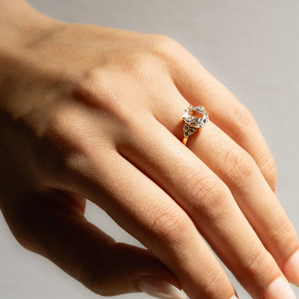 Oval white sapphire engagement ring with diamond accents in yellow gold, shown on hand.