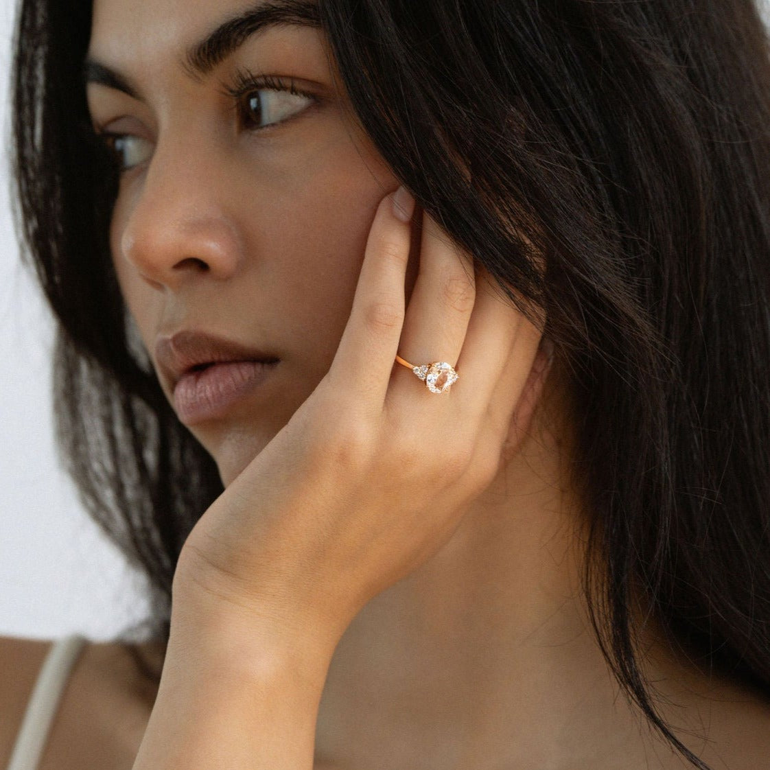 Model wearing oval white sapphire engagement ring with diamond side stones in yellow gold.