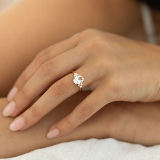 Hand wearing oval white sapphire engagement ring with diamond side stones in yellow gold.