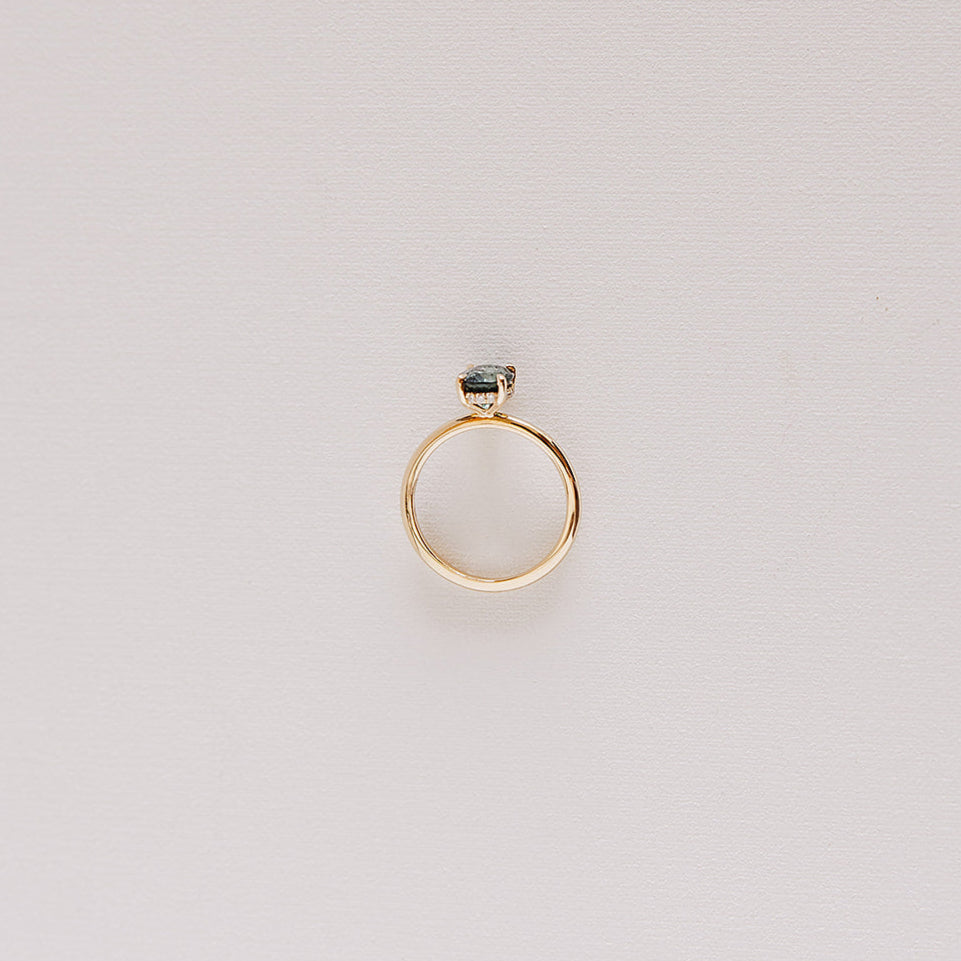 Top-down view of the Sweet Romance teal sapphire ring, highlighting the full 14k yellow gold band and a glimpse of the hidden diamond halo.