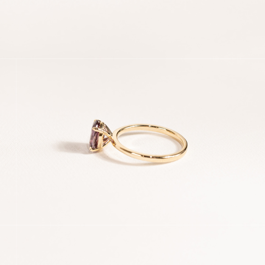 Charmed ring featuring a mauve oval sapphire in a solitaire setting on a thin 14K yellow gold band, photographed from the side against a light background.