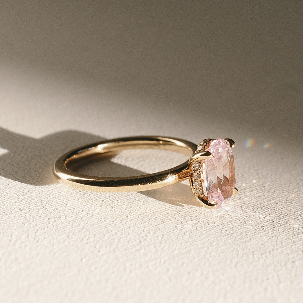 Sweet Romance solitaire ring with oval peach-pink sapphire set in 14k yellow gold, close-up side profile view.