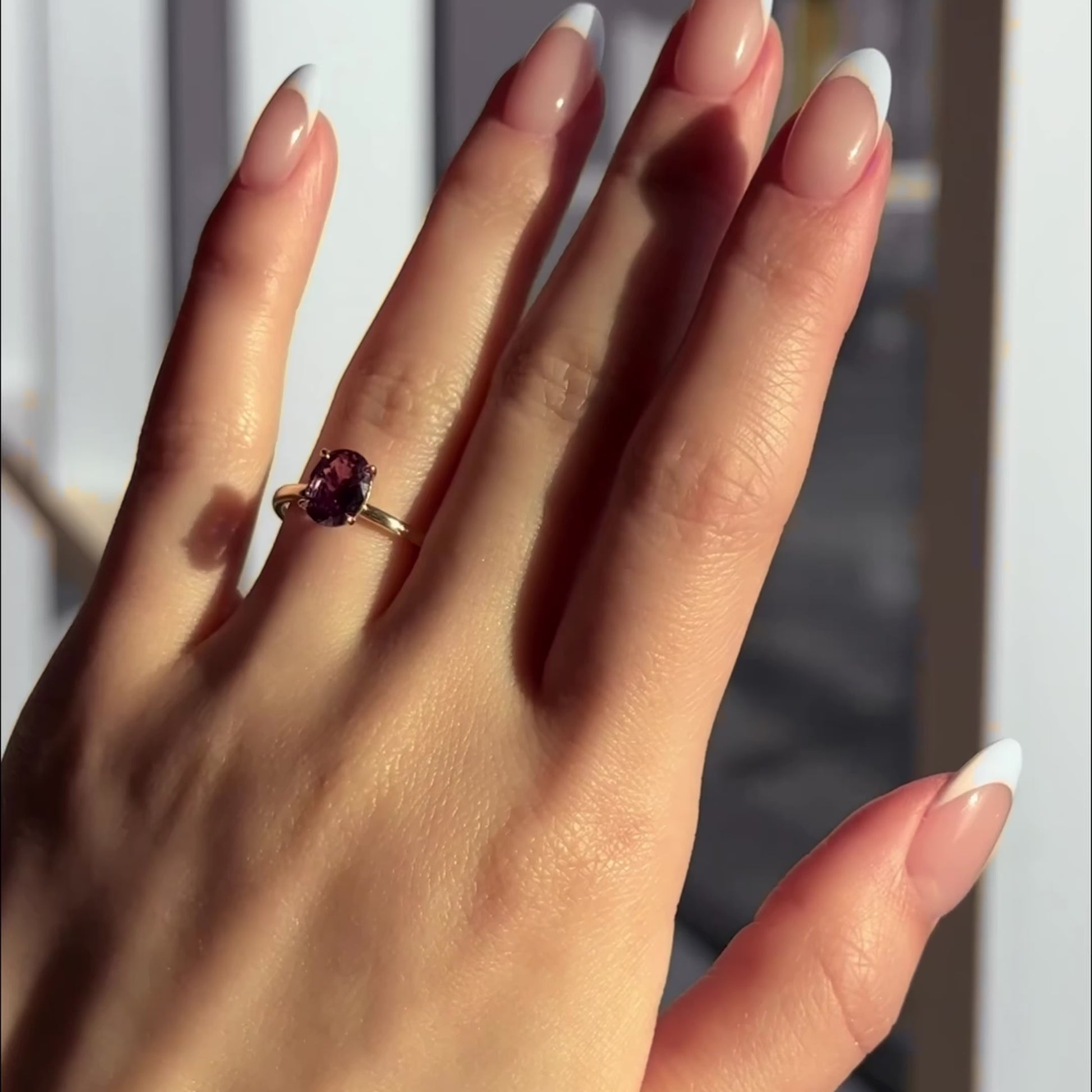 Hand wearing the Charmed ring with a mauve oval sapphire solitaire set in a 14k yellow gold band.