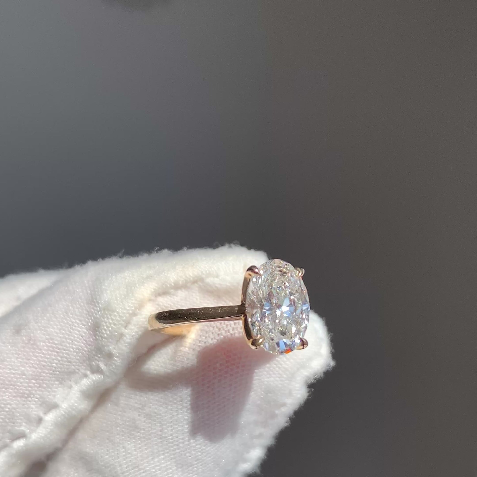 White-gloved hand showing oval solitaire lab-grown diamond engagement ring in yellow gold cathedral setting.