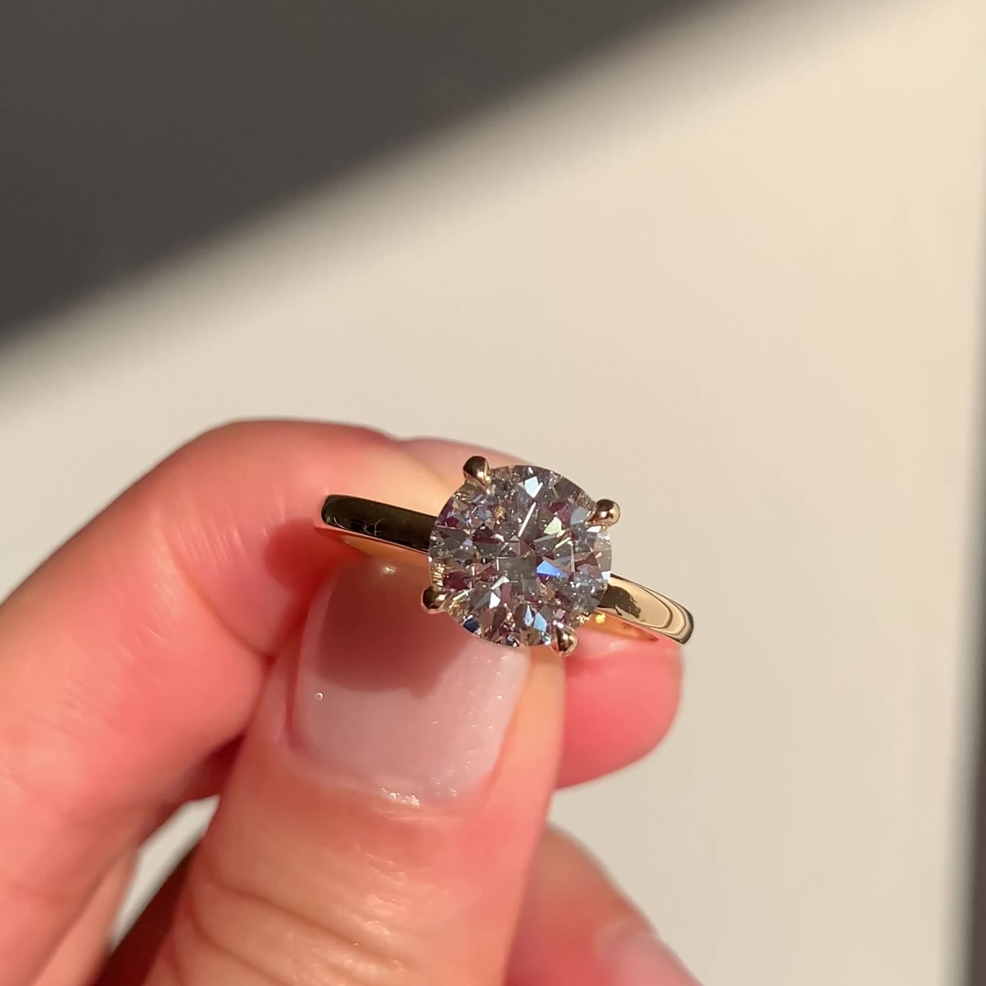 Close-up of the Delighted engagement ring, featuring a 2.01 carat round lab diamond in a six-prong 14k yellow gold solitaire setting, held between fingers in natural light.
