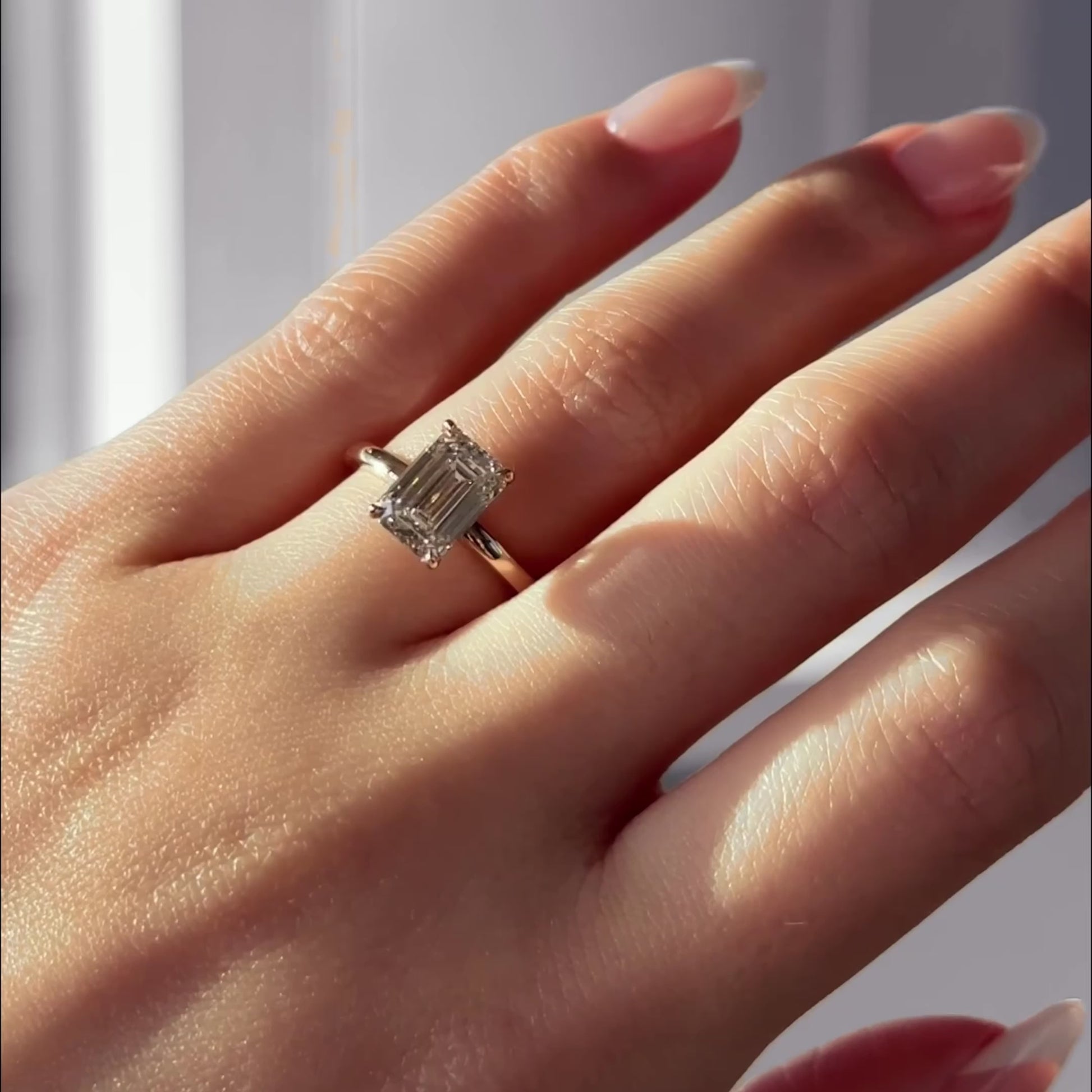 Hand wearing the Enamoured engagement ring with a 2.05 carat emerald-cut lab diamond set in a 14k yellow gold solitaire band, shown in natural light.
