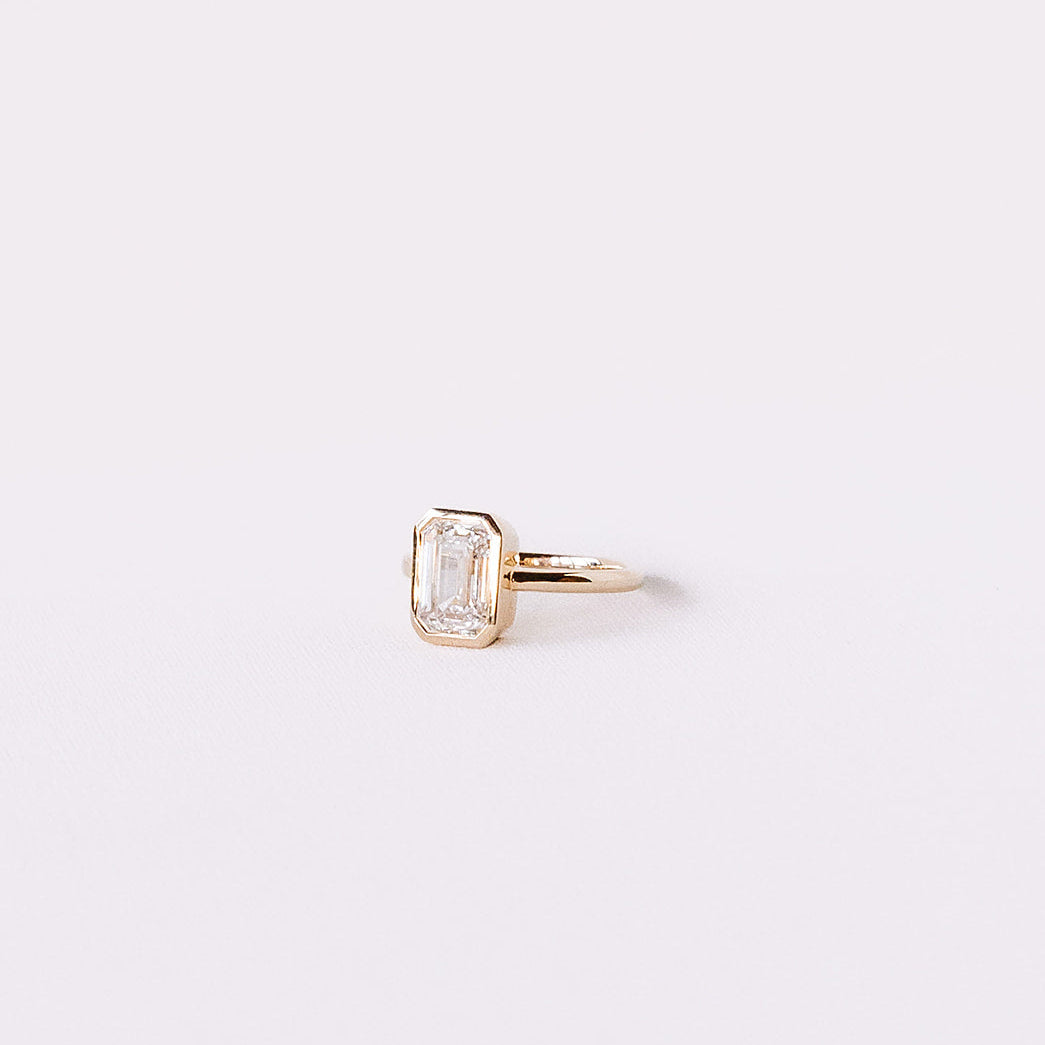 Ma Folie emerald-cut bezel lab diamond engagement ring in 14k yellow gold shown from the side highlighting the low bezel setting and slim band