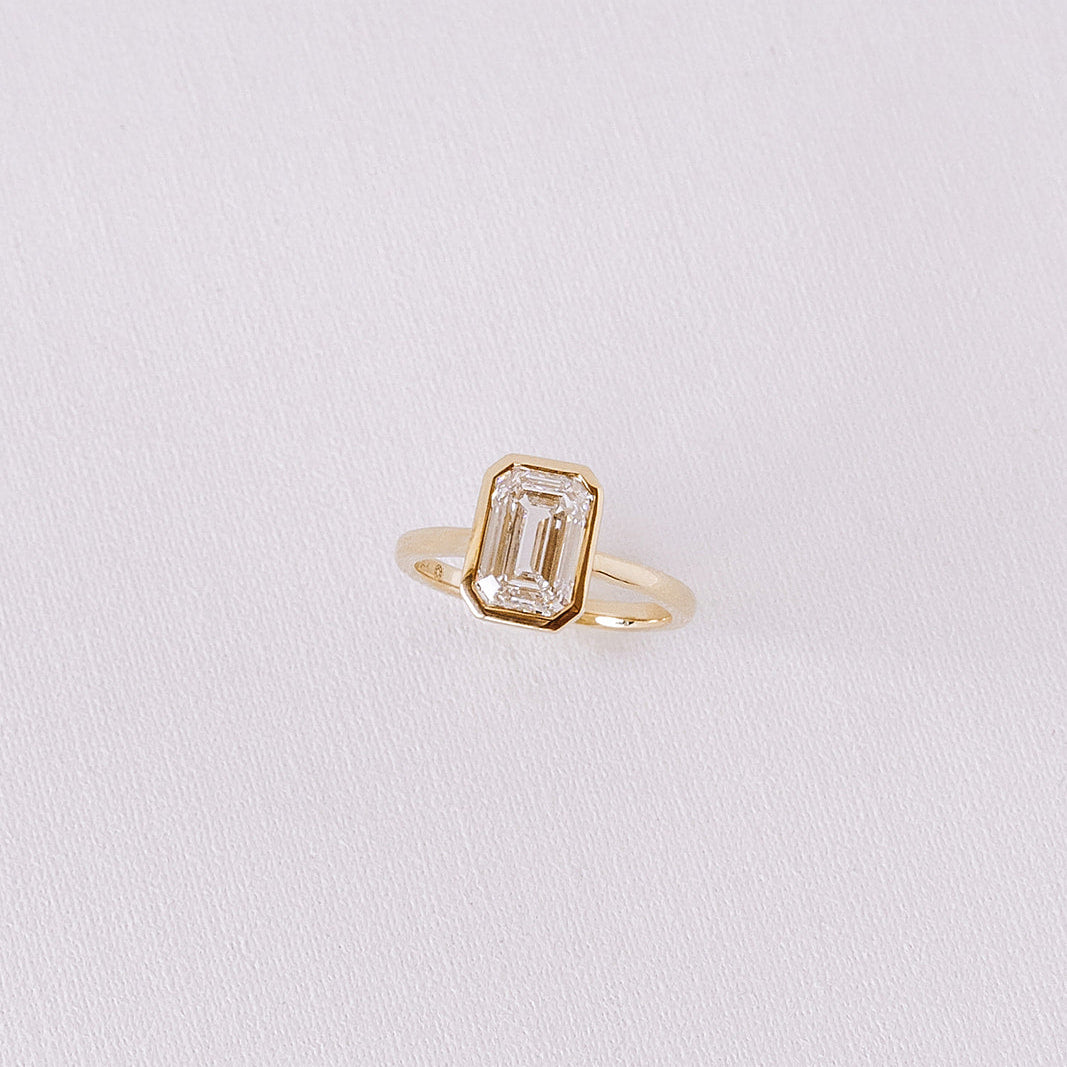Ma Folie emerald-cut bezel lab diamond engagement ring in 14k yellow gold shown at an angle highlighting the clean bezel setting and diamond facets