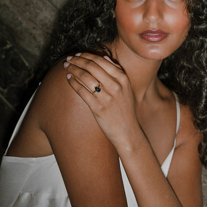 Model wearing Ma Folie’s Swell ring. A teal pear sapphire solitaire in 14k yellow gold, shown on hand against a natural textured background.