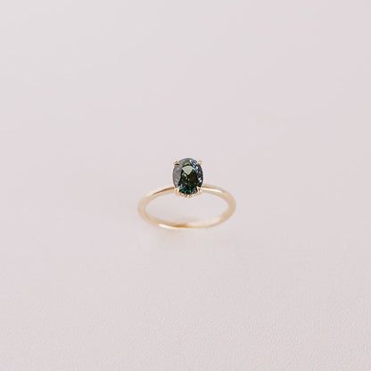 Top-down view of the Sweet Romance teal sapphire ring standing upright, showcasing the oval-cut 1.71ct sapphire and hidden diamond halo in 14k yellow gold.