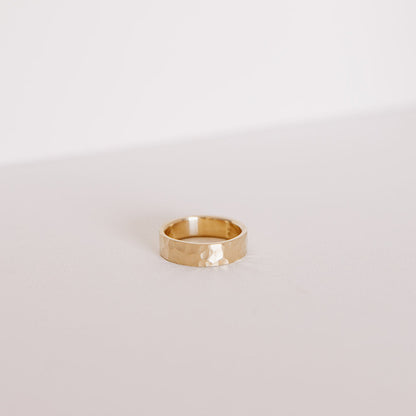 Front view of the Echo men’s wedding band in yellow gold, lying on its side to highlight the bold hammered texture and clean 6mm profile.
