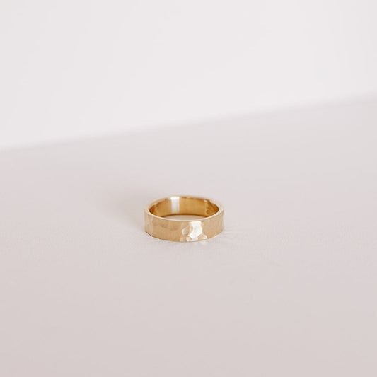 Front view of the Echo men’s wedding band in yellow gold, lying on its side to highlight the bold hammered texture and clean 6mm profile.