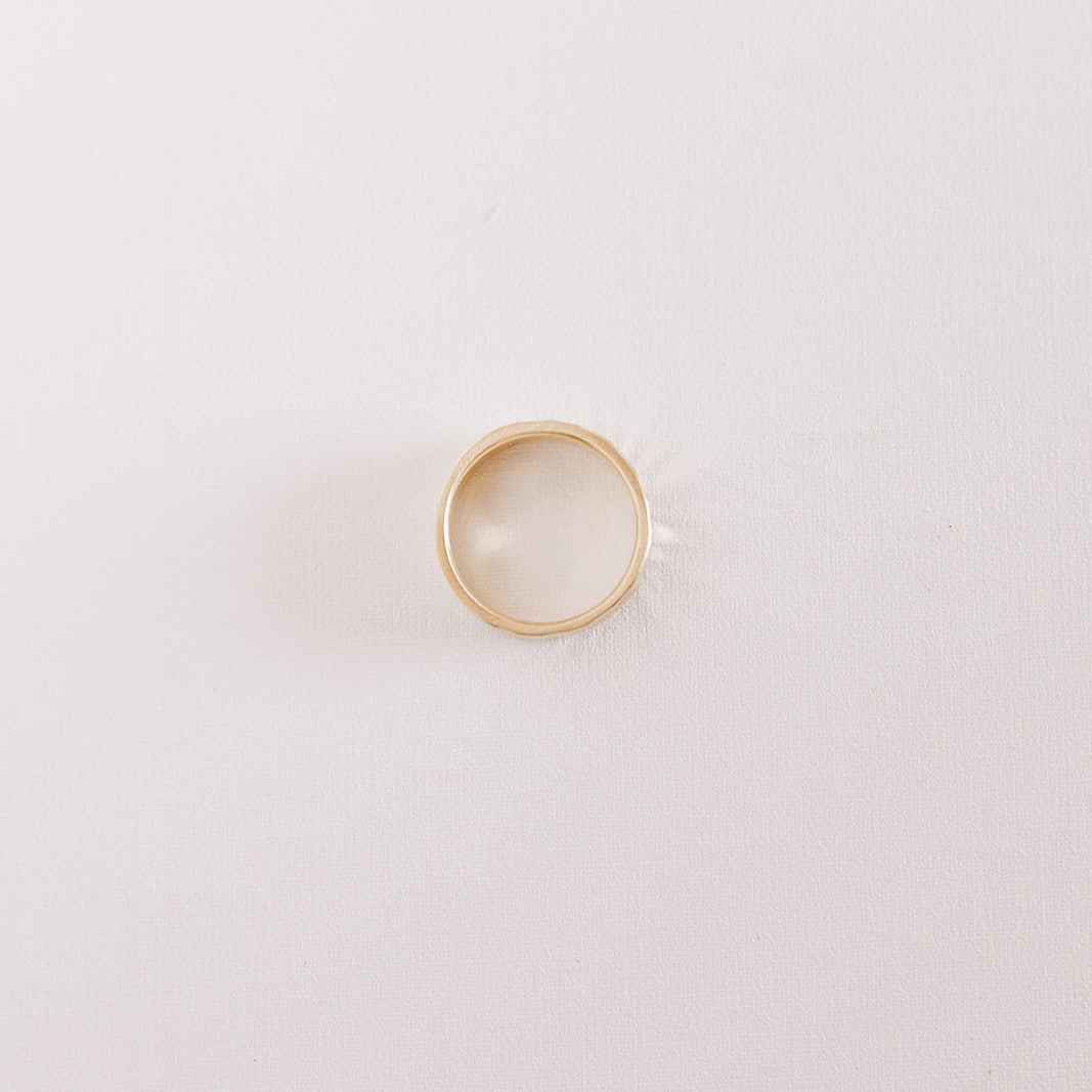 Top view of the Echo men’s wedding band lying on its side, showing the hammered texture and warm yellow gold finish against a soft neutral background.