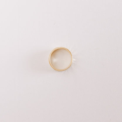 Top view of the Echo men’s wedding band lying on its side, showing the hammered texture and warm yellow gold finish against a soft neutral background.