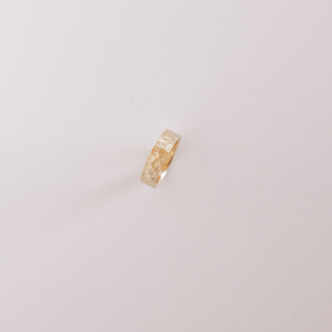 Above view of the Echo men’s wedding band standing on its edge, showcasing the hammered texture and warm yellow gold tone under soft studio lighting.