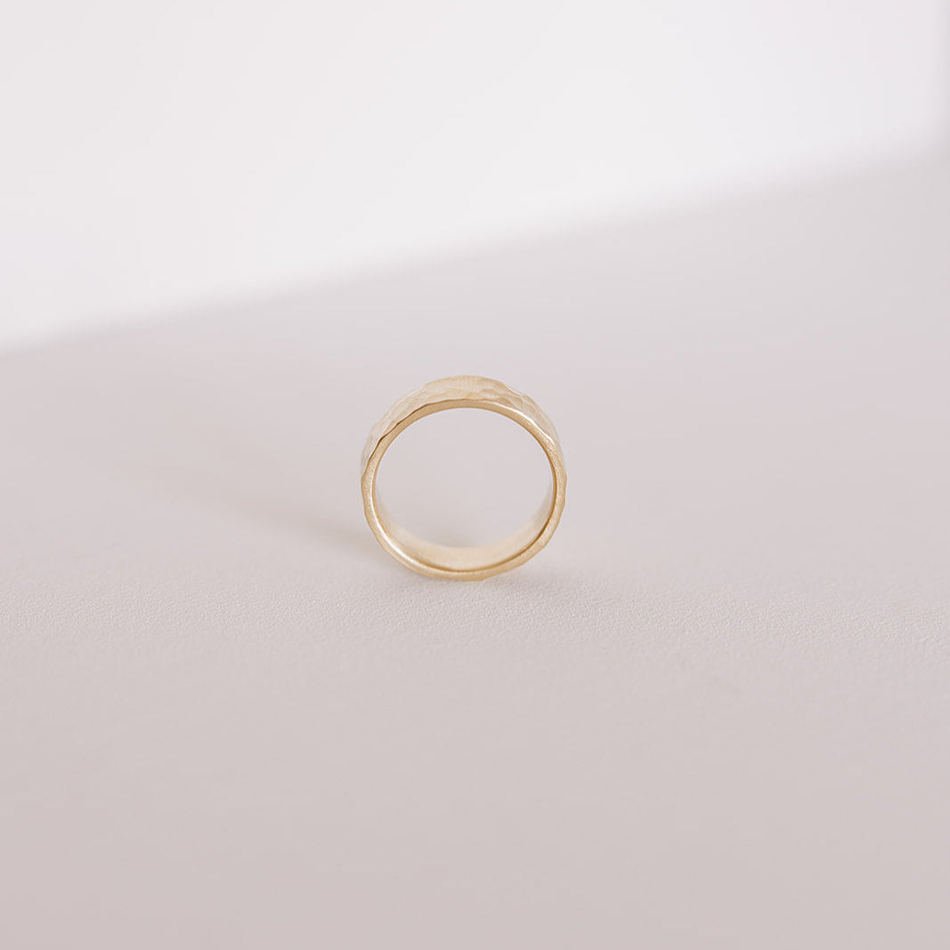 Close-up of the Echo men’s wedding band standing on its edge, highlighting the hand-hammered surface and warm yellow gold against a soft neutral backdrop.