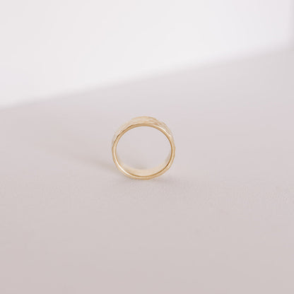 Close-up of the Echo men’s wedding band standing on its edge, highlighting the hand-hammered surface and warm yellow gold against a soft neutral backdrop.