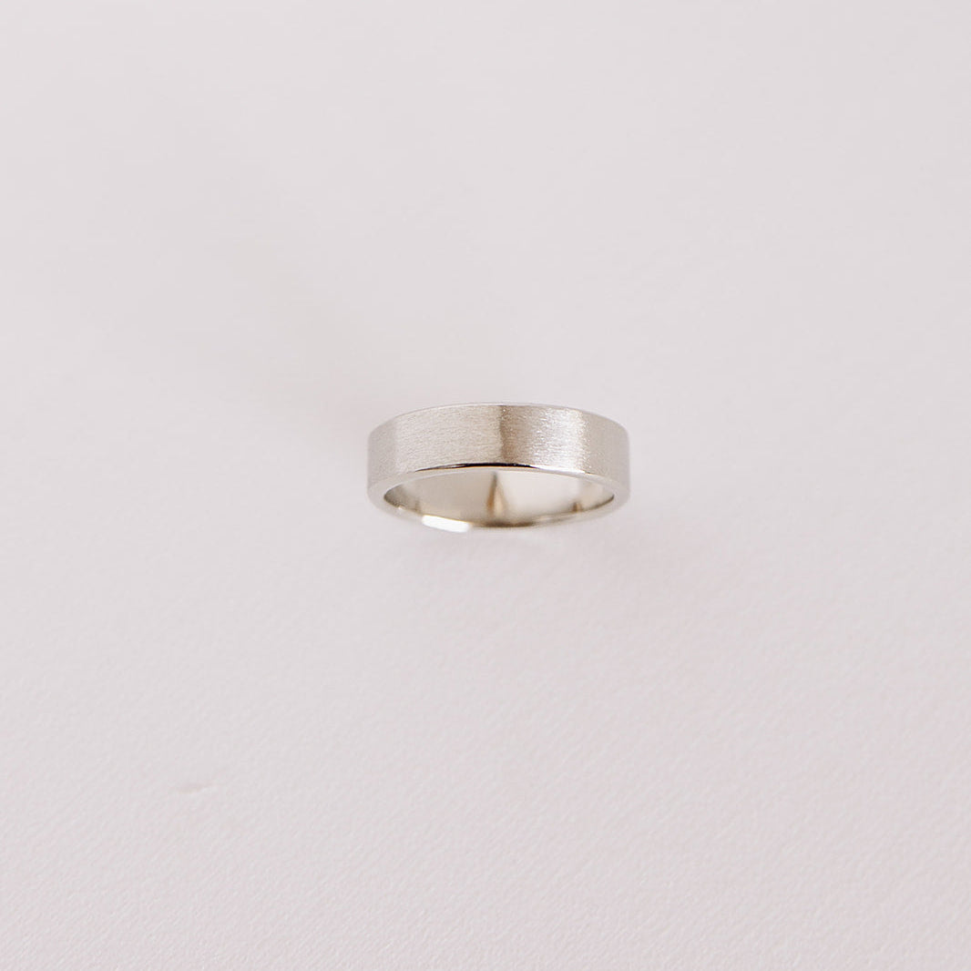 Above view of the Vow (Brushed) men’s wedding band standing on its side, showcasing the brushed 14k white gold finish against a soft background.